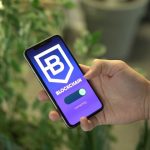 Mão segurando um smartphone que exibe uma aplicação de blockchain.