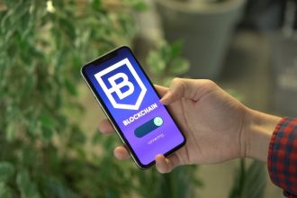 Mão segurando um smartphone que exibe uma aplicação de blockchain.
