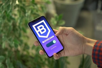 Mão segurando um smartphone que exibe uma aplicação de blockchain.