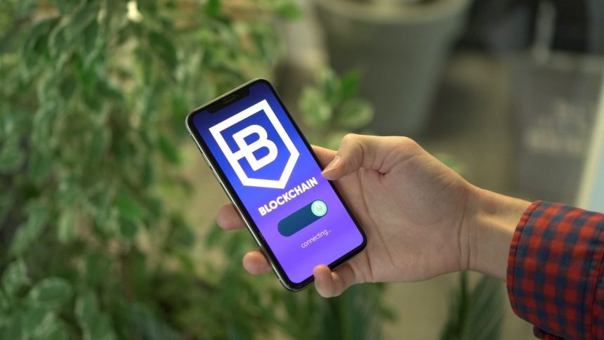 Mão segurando um smartphone que exibe uma aplicação de blockchain.