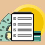 Tablet com marcas de verificação ao lado de cédulas e cartão de crédito, representando a aprovação digital de pagamentos.