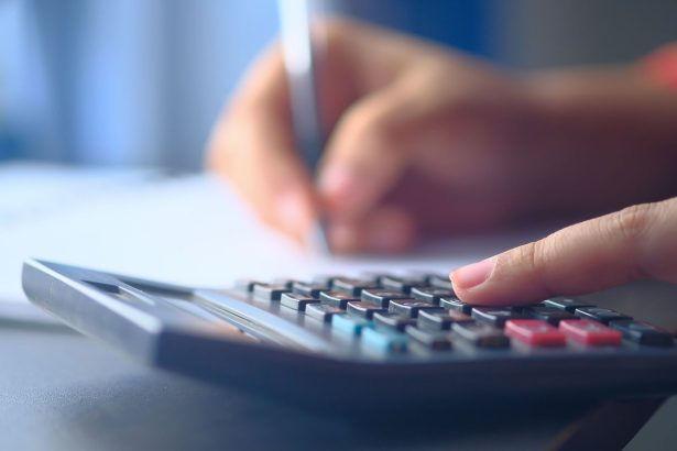 Mãos fazendo cálculos em uma calculadora e anotando informações para planejar o orçamento doméstico.