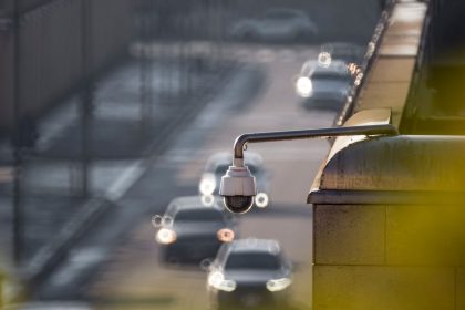 Câmera de vigilância monitorando uma via urbana movimentada, com veículos desfocados ao fundo.