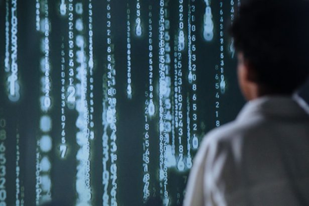 Pessoa observa números luminosos em uma tela, representando tecnologia e processamento de dados.