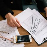 Pessoa analisa formulários fiscais, documentos e uma calculadora sobre uma mesa.