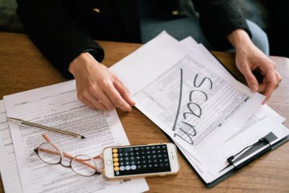 Pessoa analisa formulários fiscais, documentos e uma calculadora sobre uma mesa.