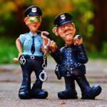 Agentes policiais uniformizados ao lado de uma viatura, em uma imagem ilustrativa sobre segurança pública.