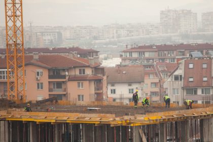 Trabalhadores atuam em um canteiro de obras urbano, com edifícios ao fundo.